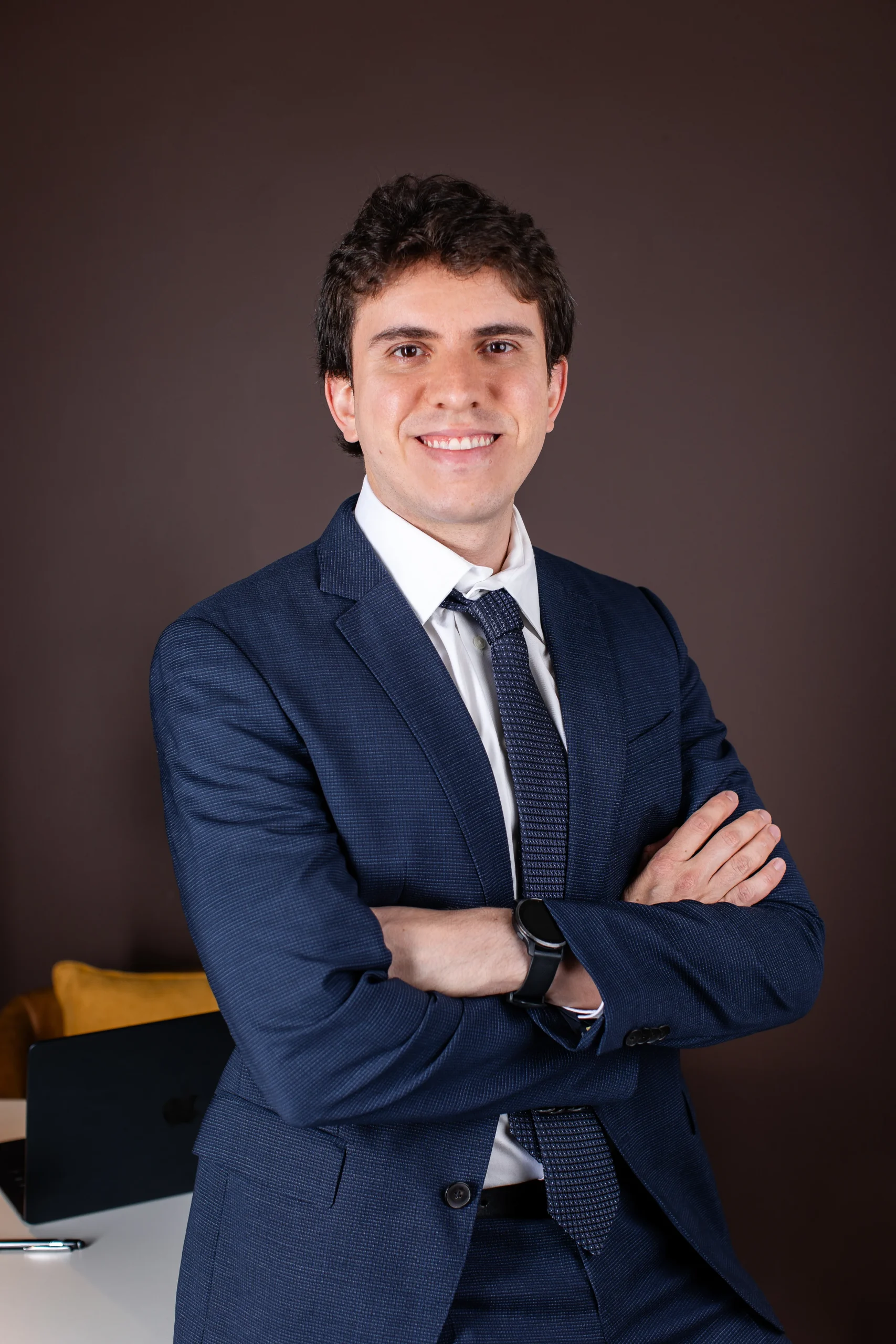 Dr. Matheus Massahud sorrindo, de terno azul e braços cruzados, em retrato profissional