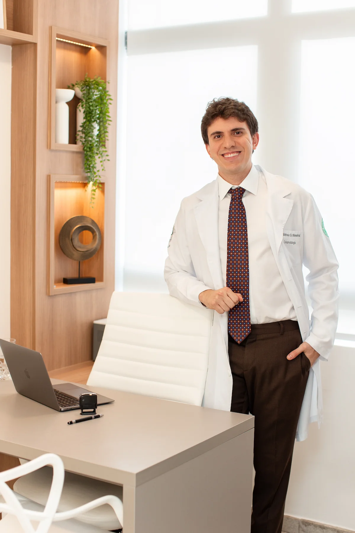 Dr. Matheus Massahud sorrindo, usando jaleco branco, em seu consultório.