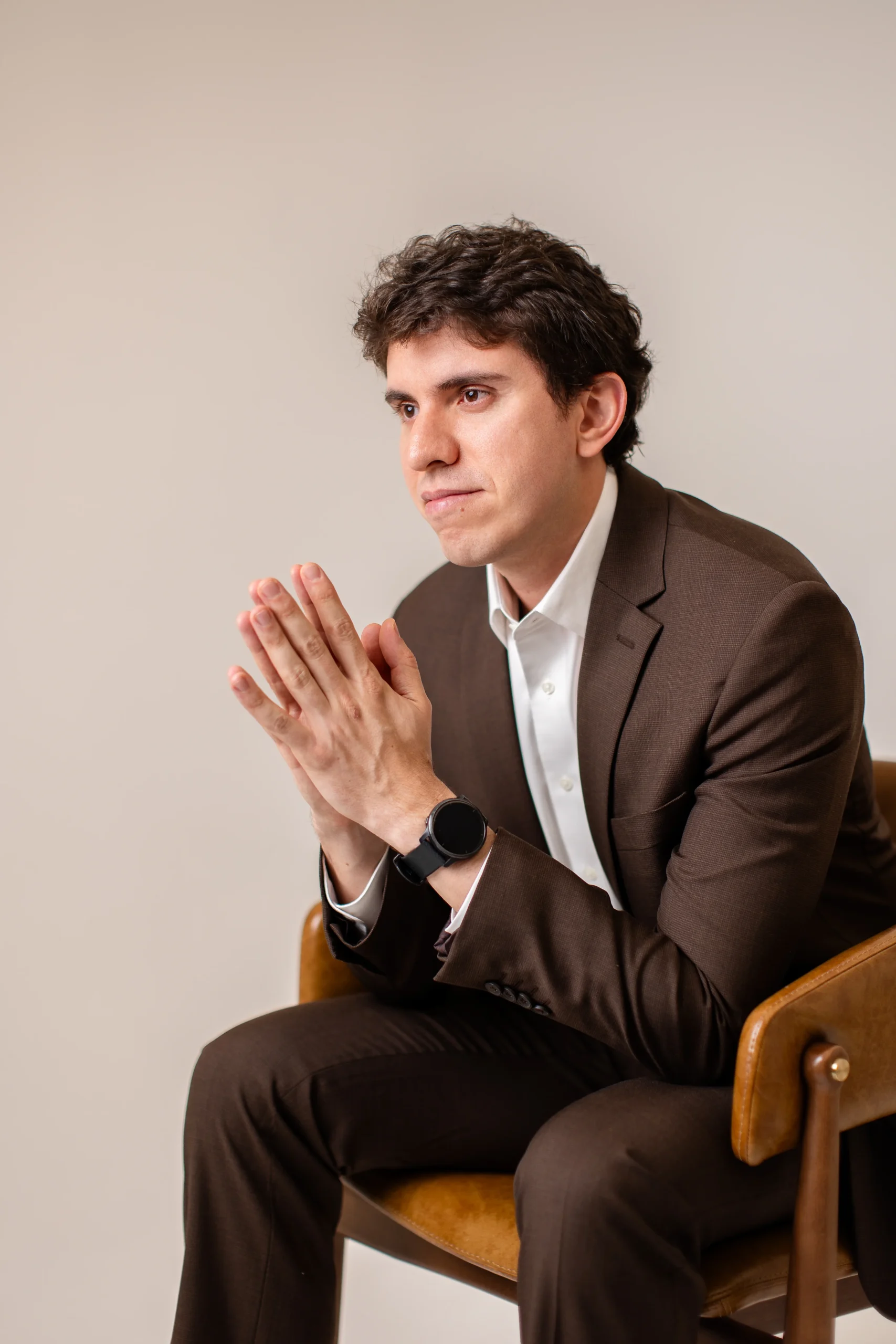 Dr. Matheus Massahud sentado, de terno, com as mãos unidas com fundo claro.